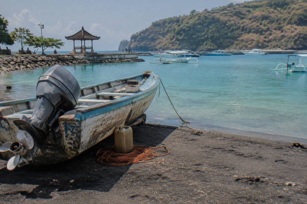 A wooden fast boat with an outboard engine resting on sand beside calm turquoise water