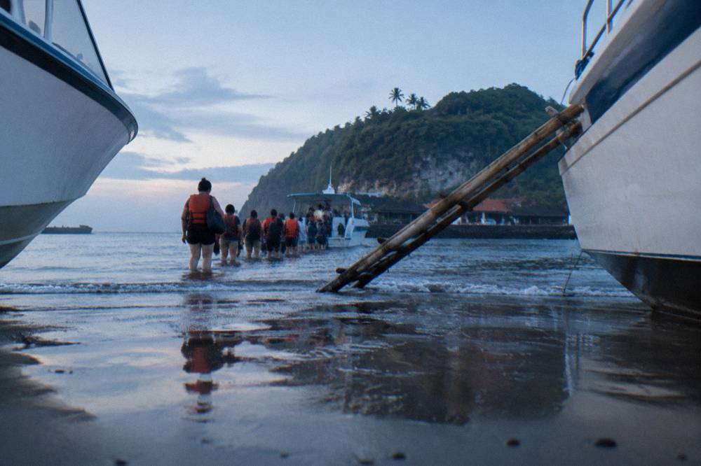 Fast boats lined up along a beachfront departure strip with passengers waiting to board