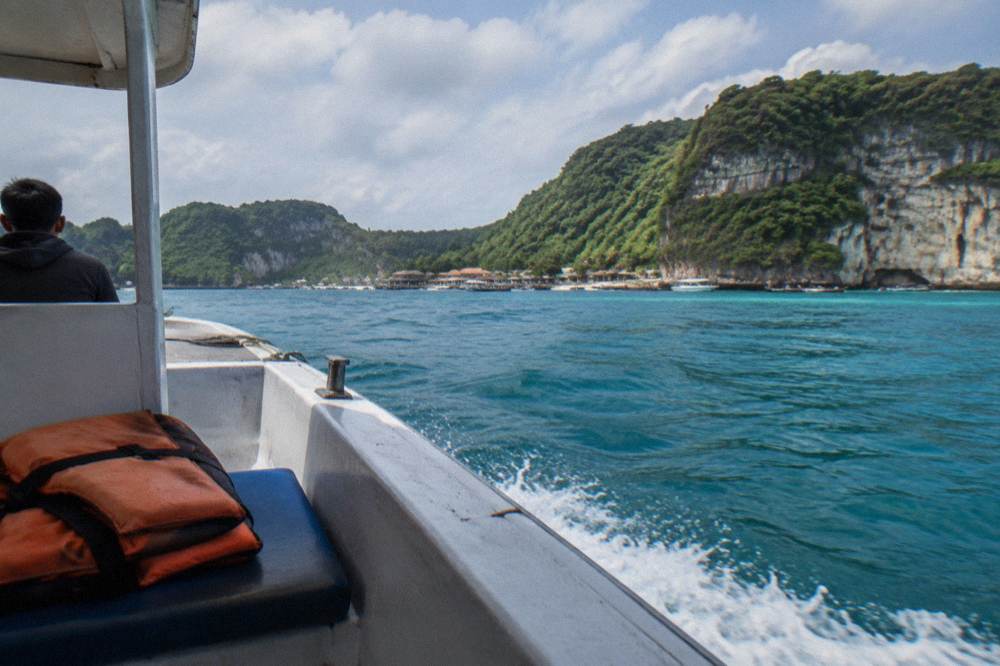 A passenger ferry crossing open turquoise water toward green cliffs under a partly cloudy sky