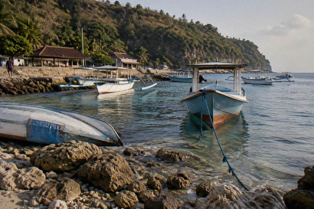 Small boats moored in clear water beside a rocky shoreline on Nusa Penida
