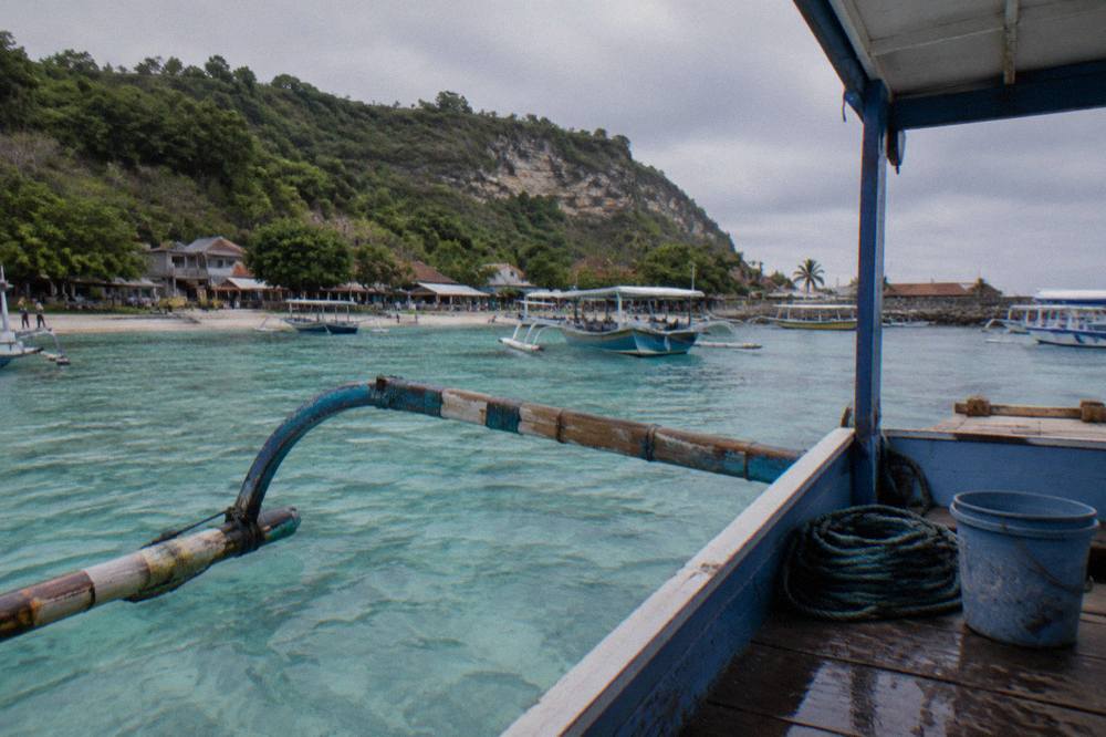 A wooden snorkelling boat anchored over clear shallow water near a Nusa Penida bay
