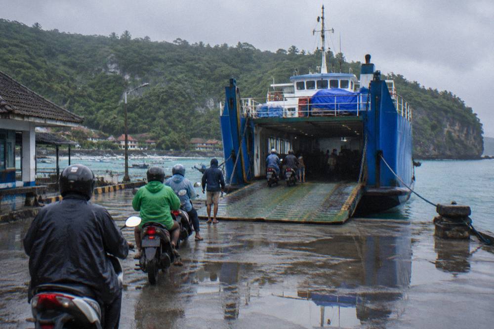 A large vehicle ferry docked at a Bali port with trucks and scooters waiting to board