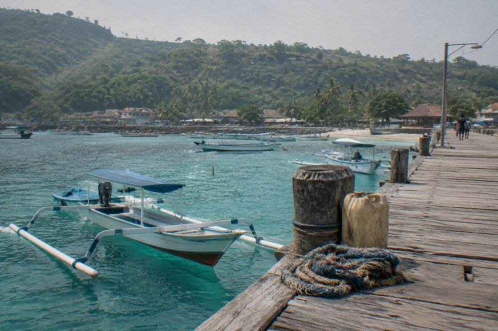 A wooden jetty at a Nusa Penida harbour with small boats moored in clear turquoise water