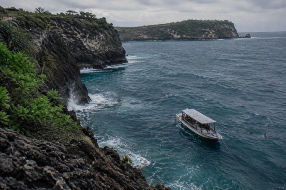 A wooden snorkeling boat anchored near cliff walls on the Nusa Penida coast