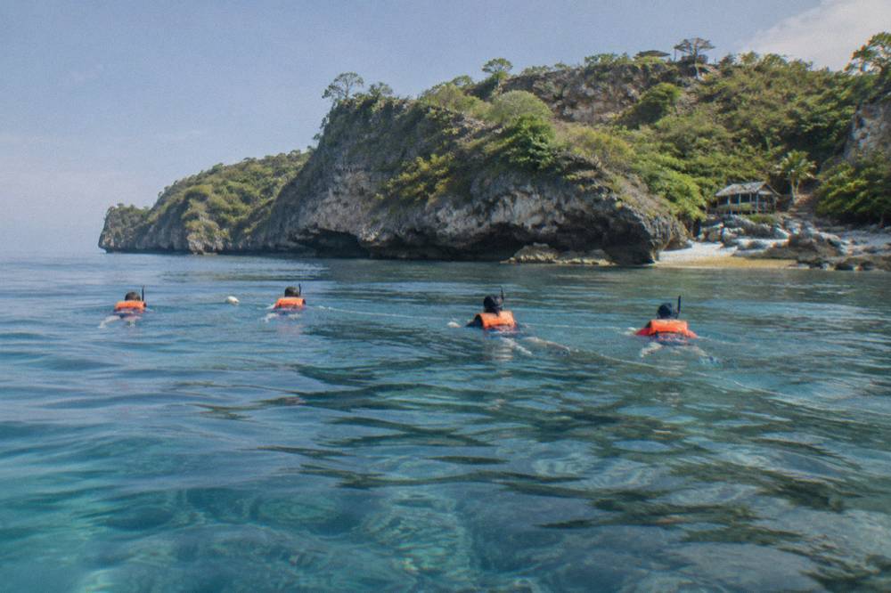 A group of snorkelers floating on the surface in a line behind a guide
