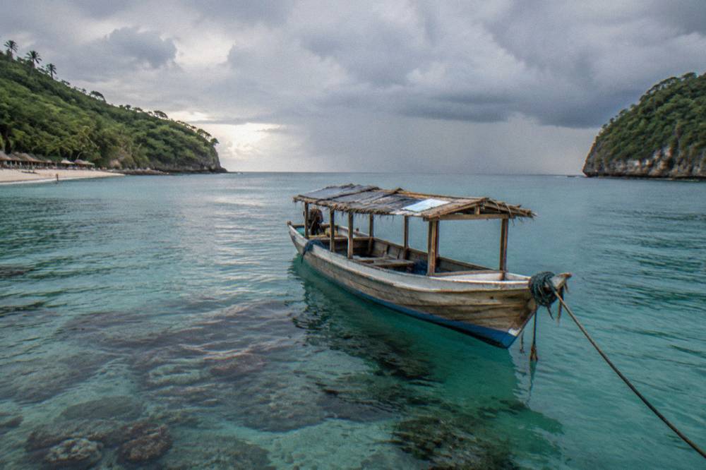 A calm turquoise bay with a snorkel boat anchored over coral reef and green headlands on either side