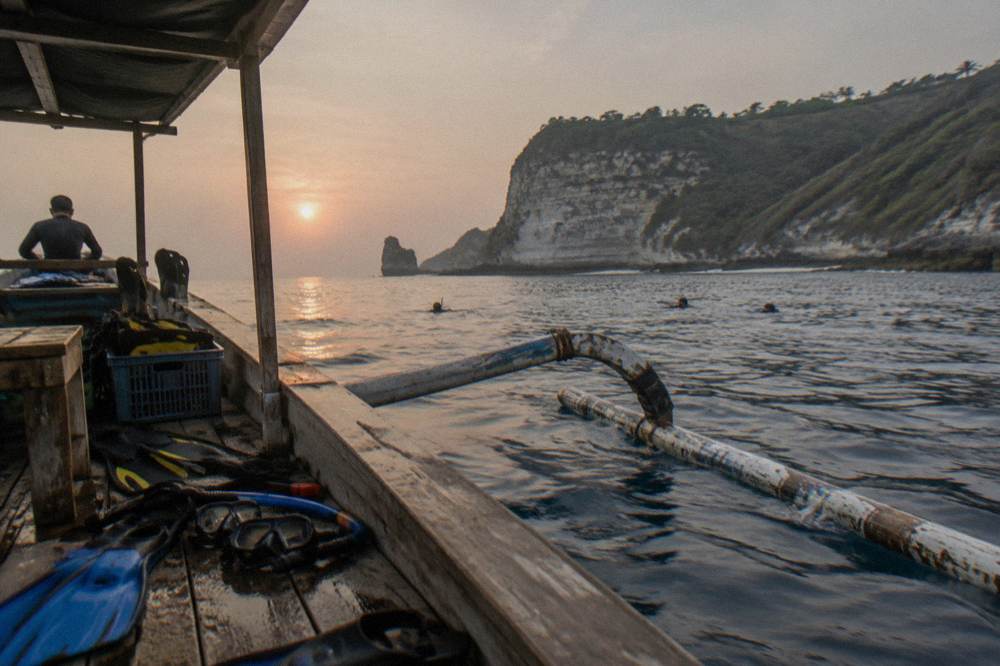 A wooden snorkel boat with gear on board floating near a rocky headland on a clear day