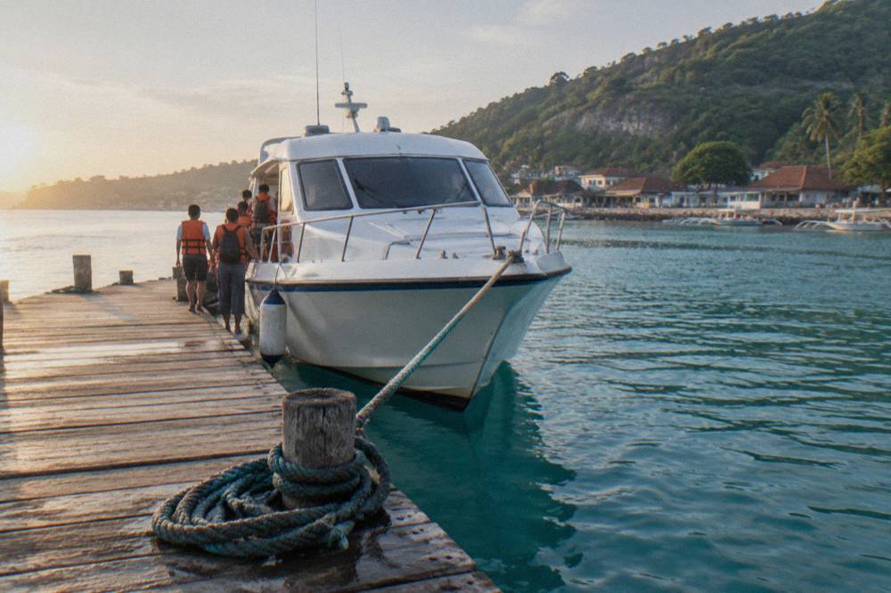 A fast boat moored at a wooden jetty with passengers boarding on a calm morning