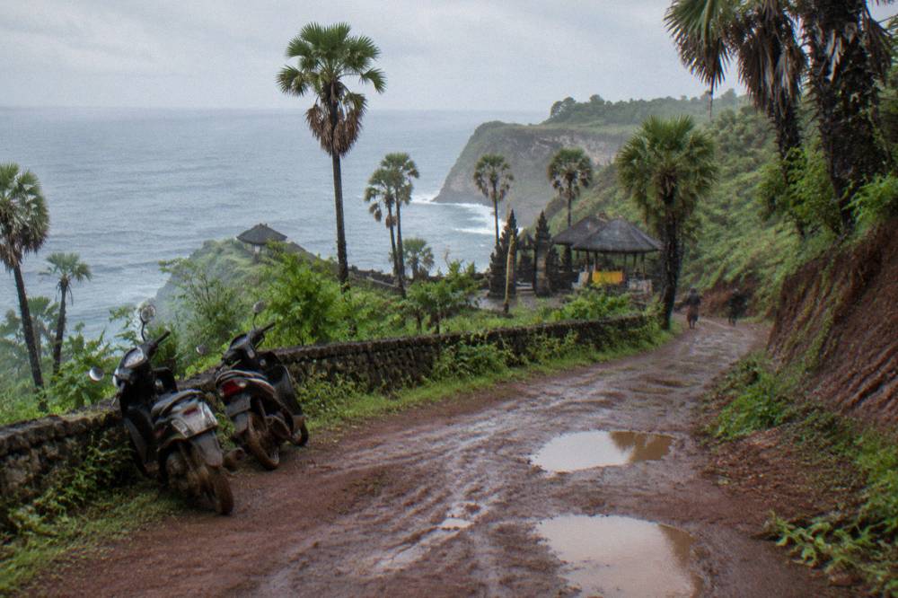 A steep coastal road curving along a green cliffside above the sea on Nusa Penida