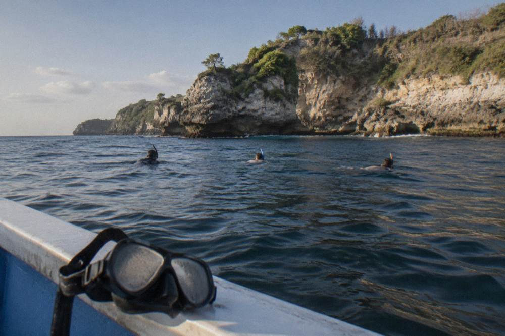 Snorkelers floating calmly above dark reef water near a rocky coastline