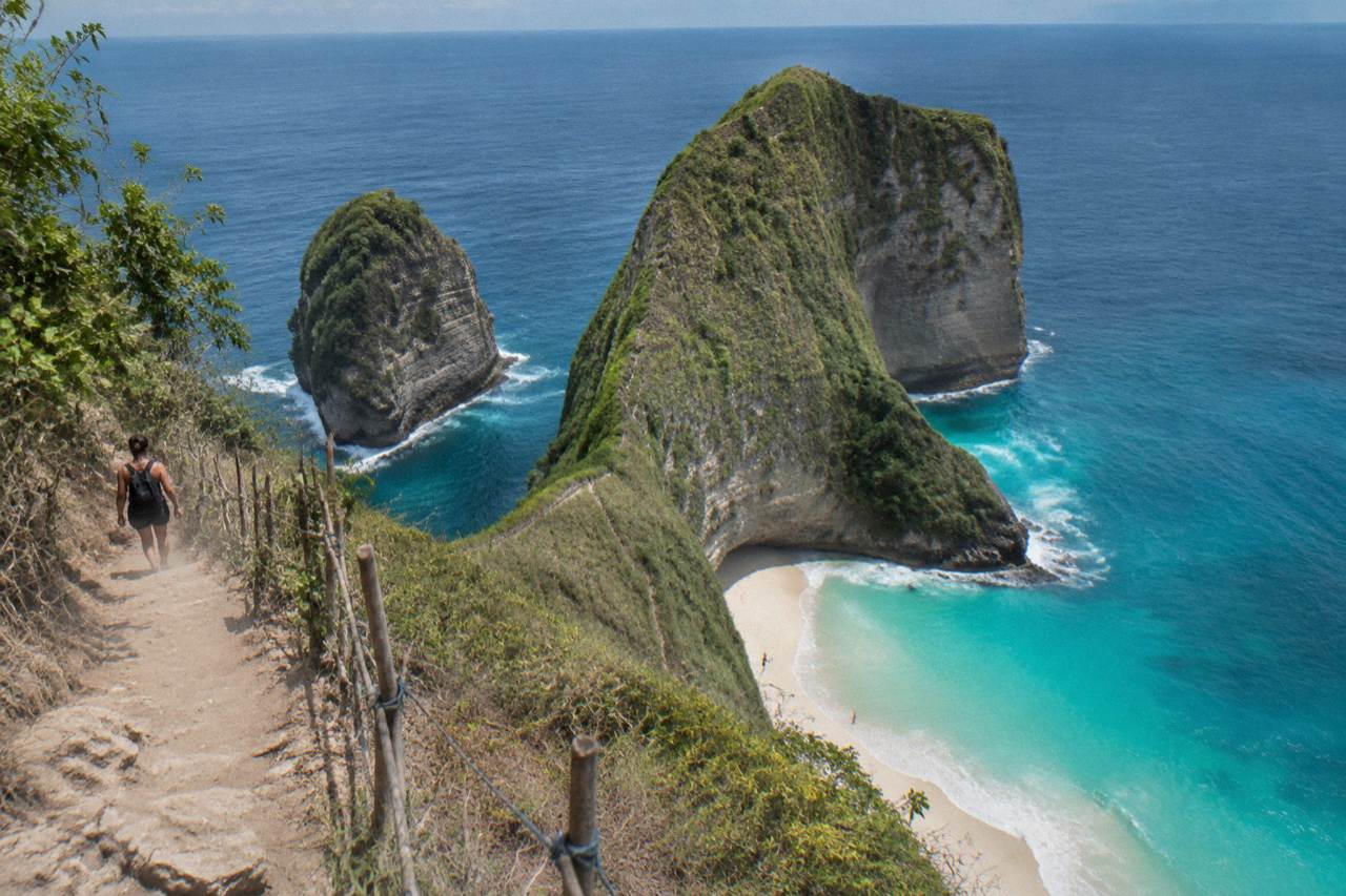 Calm turquoise water and green cliffs along the Nusa Penida coastline under a clear sky