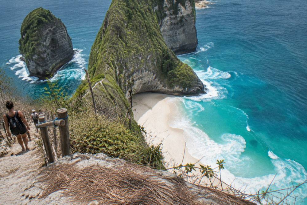 White sand cove at the base of the Kelingking cliff with turquoise waves breaking on the shore and no swimmers in the water