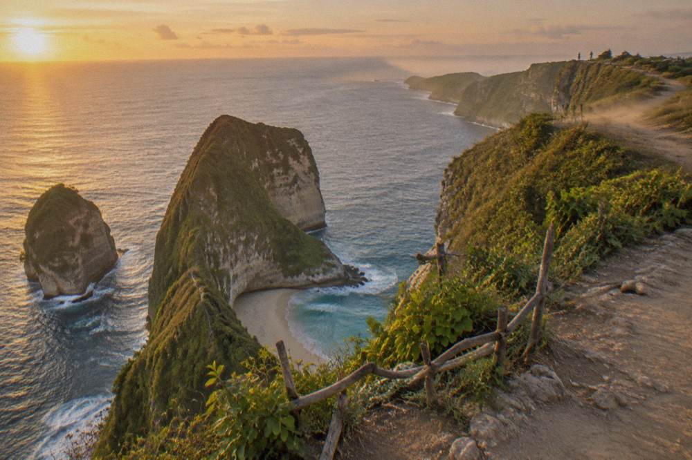 Panoramic view from the Kelingking Beach viewpoint showing the T-Rex shaped headland and the coastline of Nusa Penida in clear daylight