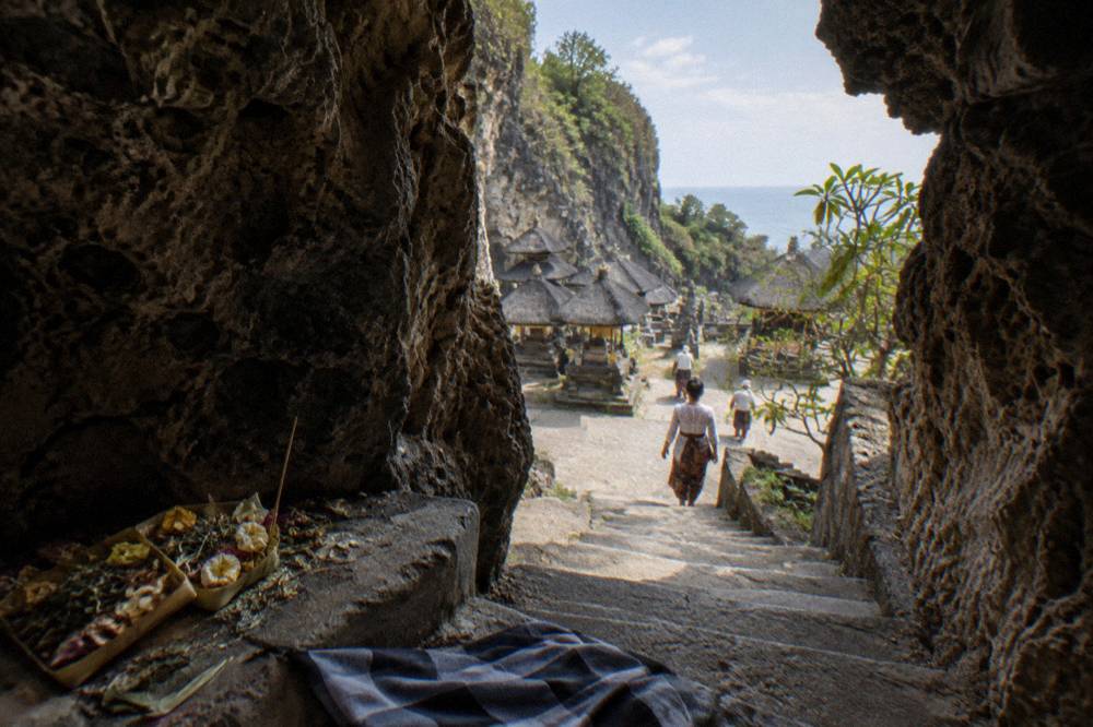 Narrow cave entrance at a Balinese temple with stone steps and offerings