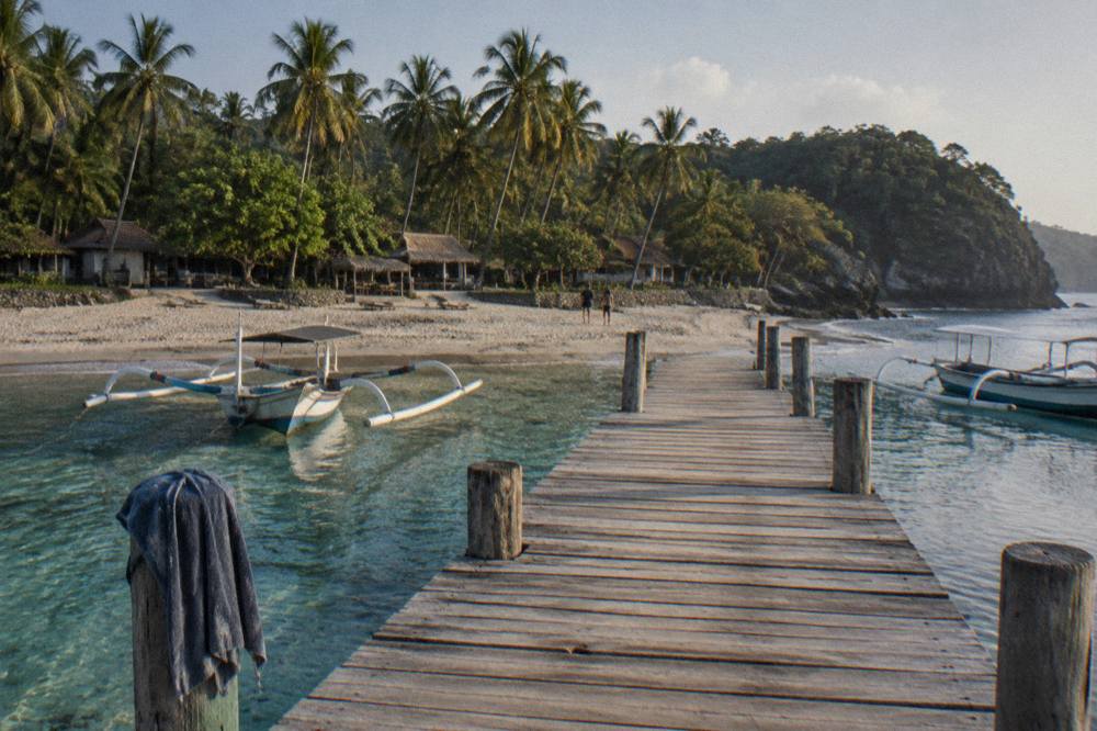 Wooden jetty over clear shallow water with boats moored along the shoreline