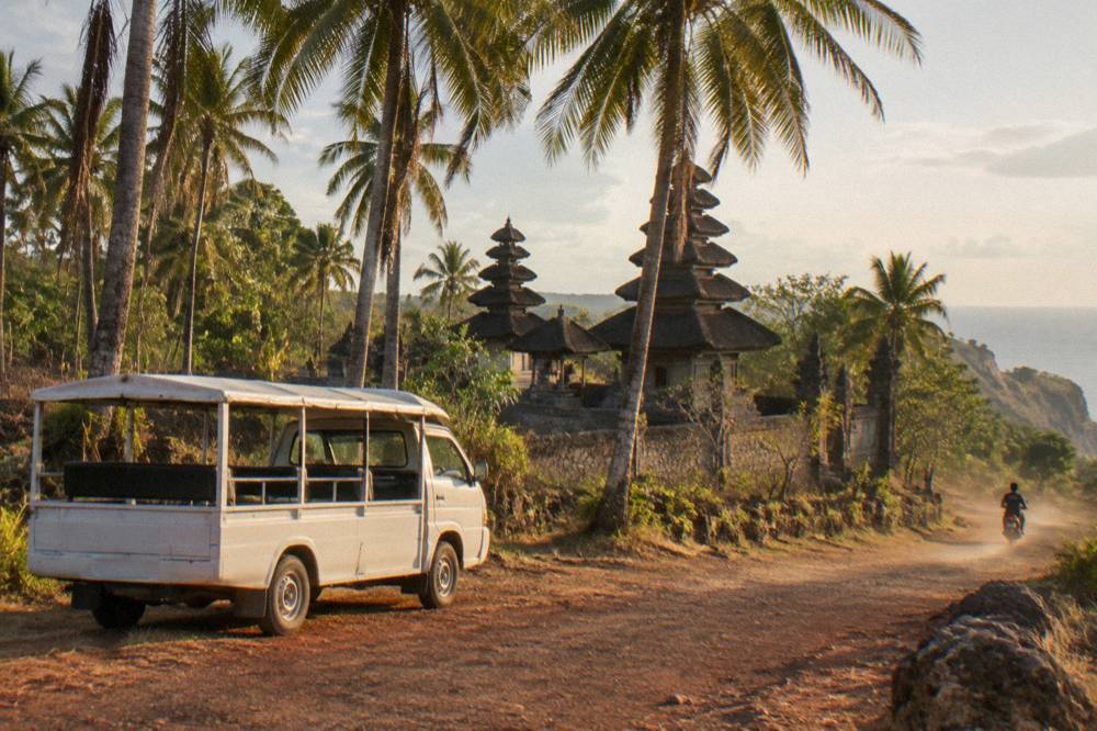 A parked open-sided minivan beside a palm-lined road near coastal cliffs