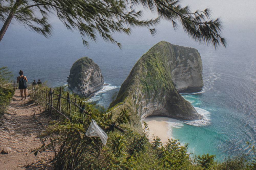 Aerial view of the Kelingking headland shaped like a dinosaur above a white sand cove
