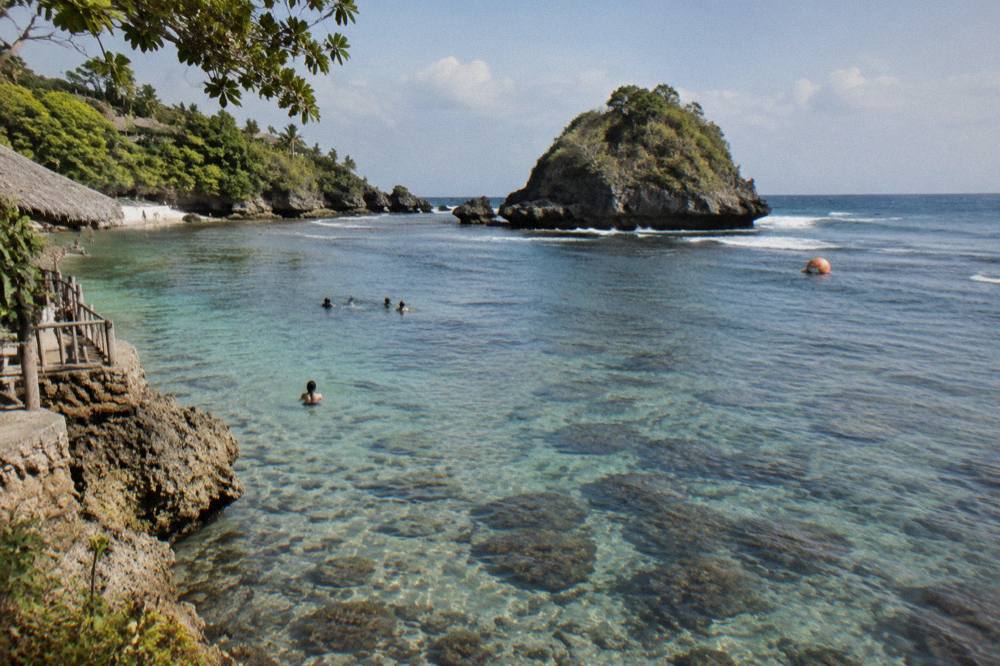 Coral reef and clear shallow water inside Crystal Bay with a rocky islet beyond