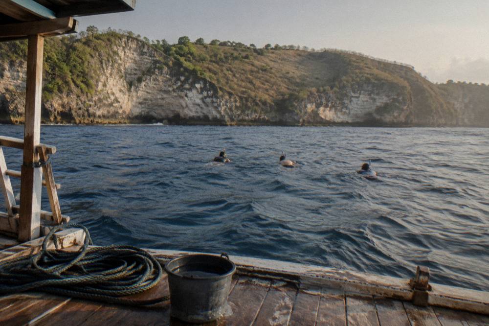 A snorkel boat anchored near rocky coastline with snorkelers in the water