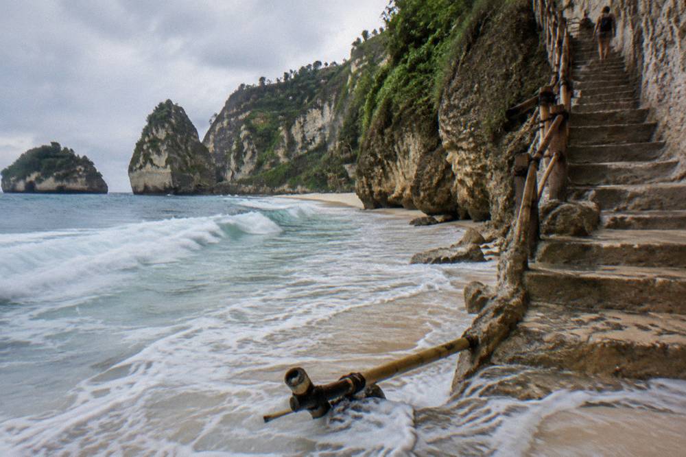 Waves breaking on white sand at the foot of a steep cliff staircase
