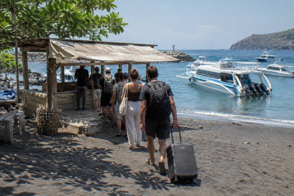 Ticket counter and queued travellers on a beachfront next to moored fast boats