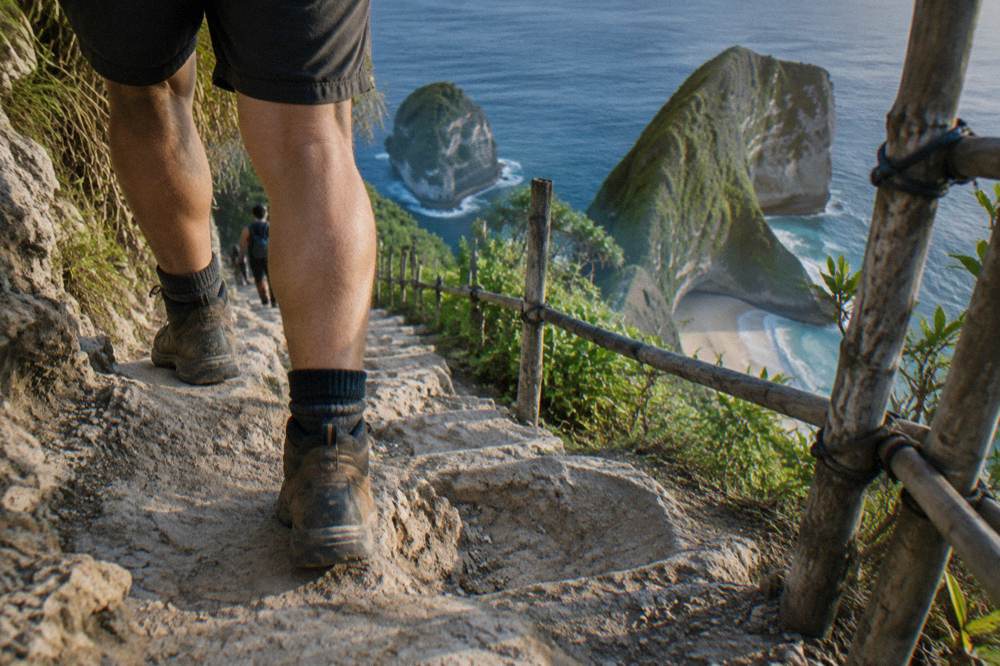 Close-up of a hiker's sturdy shoes on the rocky Kelingking trail with ocean in background