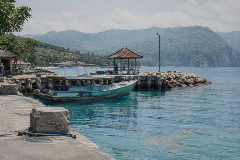 A wooden fast boat moored at a harbour with calm turquoise water and hills in the distance