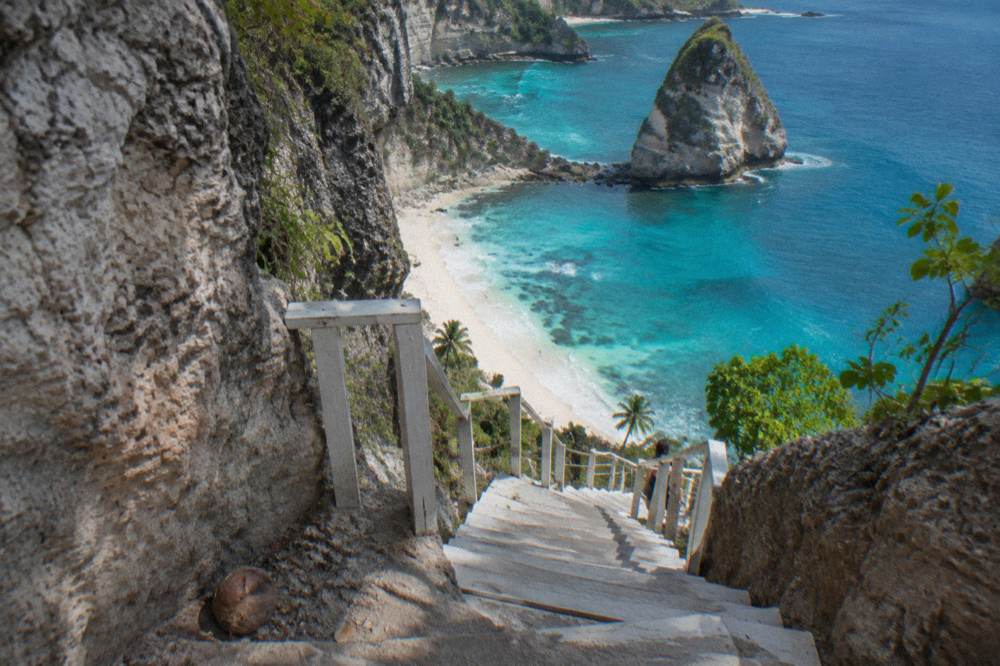 A white sandy beach below tall limestone cliffs with wooden staircases cut into the rock
