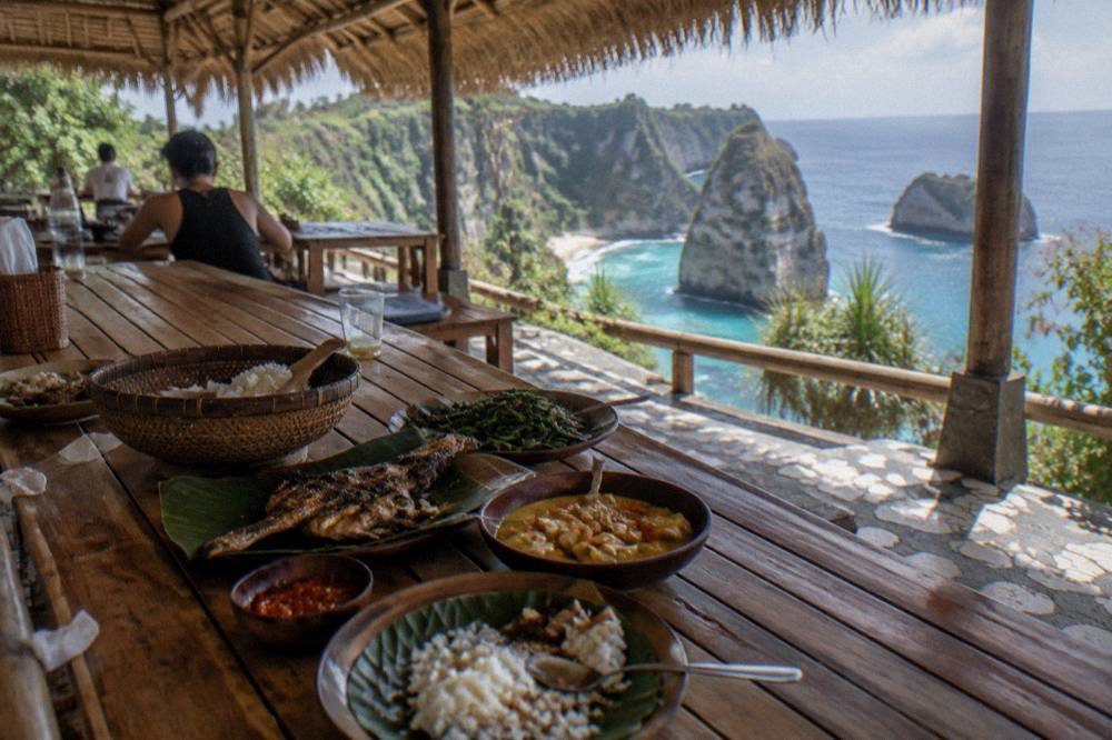 A long wooden table with Indonesian dishes served for lunch at an open-air beachside restaurant