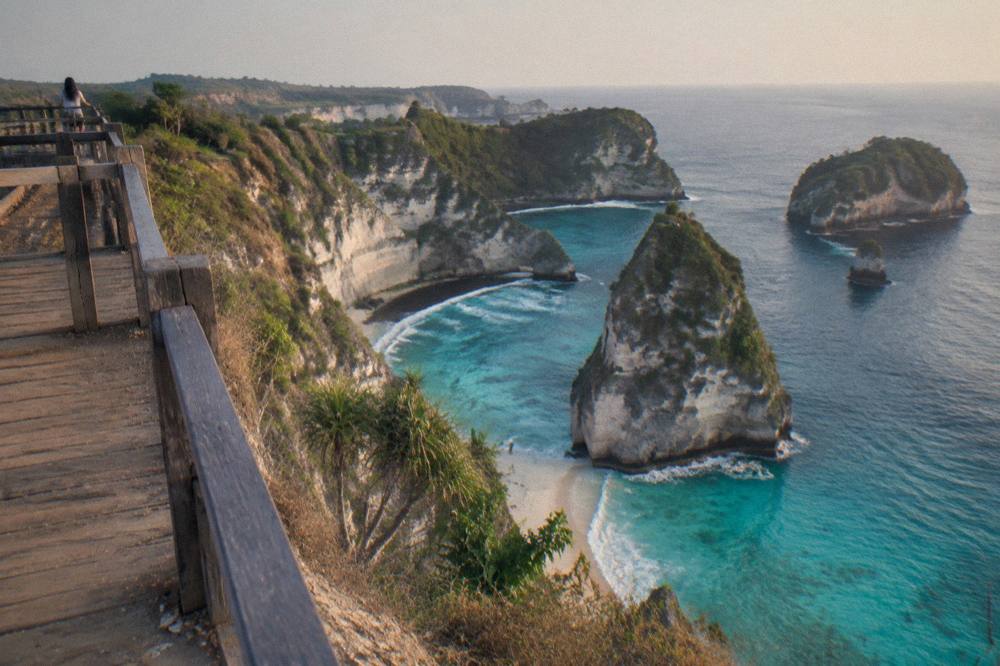 A viewpoint platform above a tall green cliff dropping into a curved turquoise bay