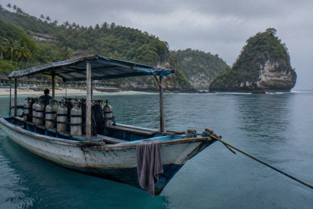 A dive boat moored above clear blue water near rocky coastline