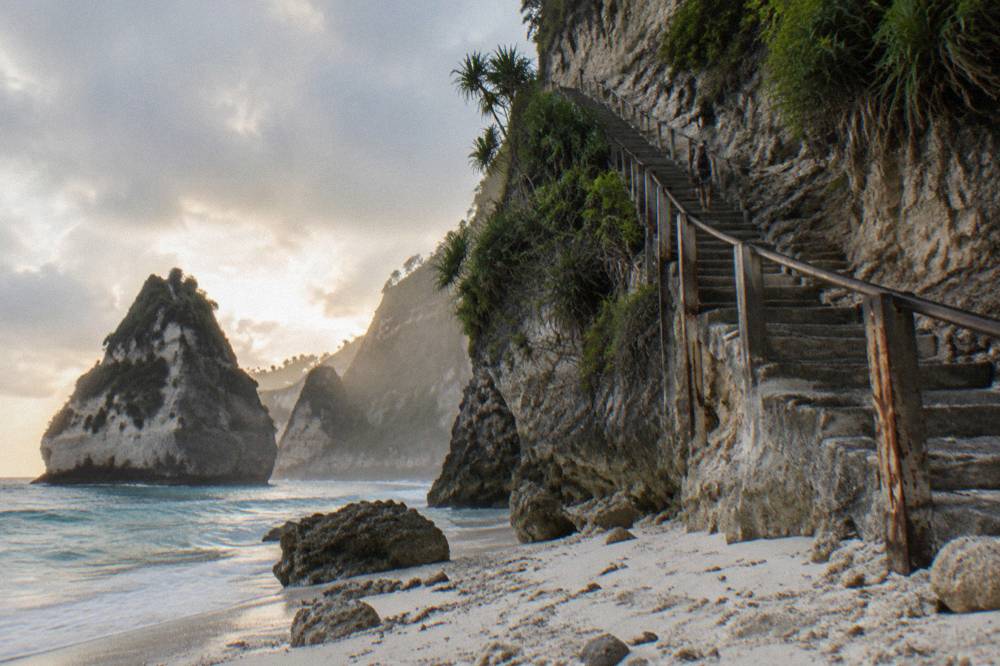 Long concrete staircase descending a cliff face toward a white sand beach