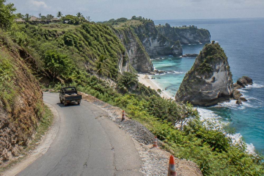 Narrow coastal road on Nusa Penida winding along green cliffs above the sea