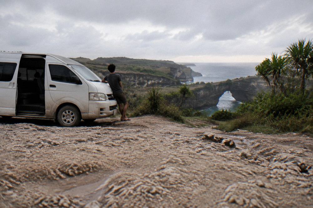 Tour van parked at a cliff viewpoint overlooking the sea on Nusa Penida