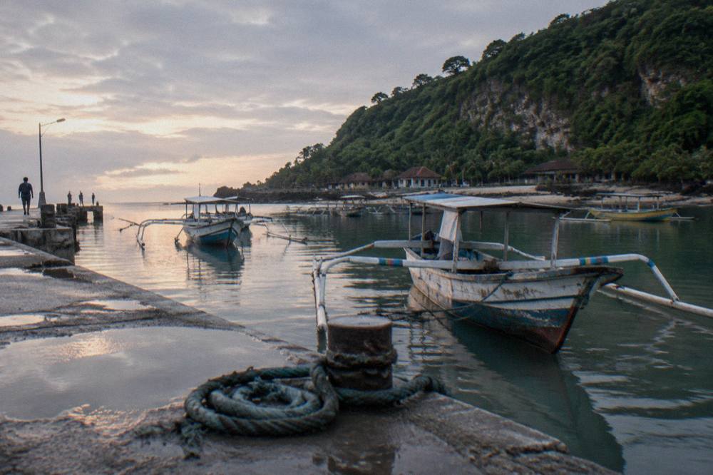 A wooden pier at a Nusa Penida harbour with moored boats and calm morning water