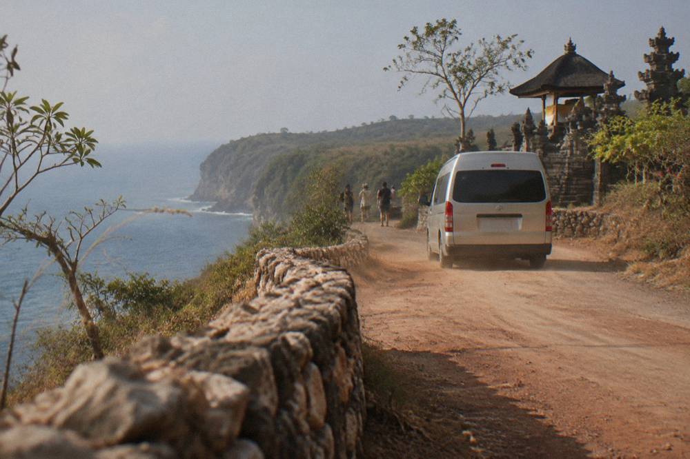 An air-conditioned tour van parked on a coastal road above the sea on Nusa Penida