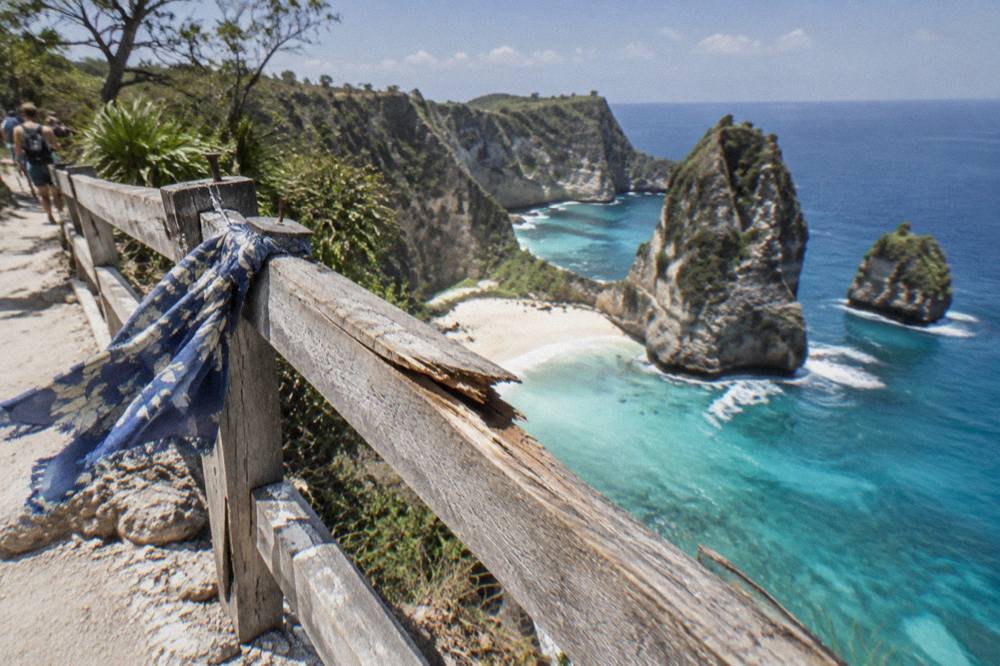 Wooden railing at a cliff edge above a turquoise bay on Nusa Penida