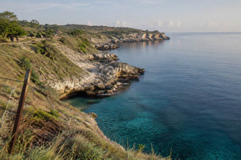 Calm dry-season sea along a limestone cliff coastline under clear sky