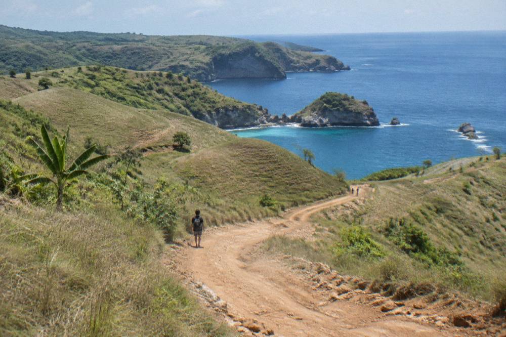 A winding coastal road on Nusa Penida with dry hills and sea beyond