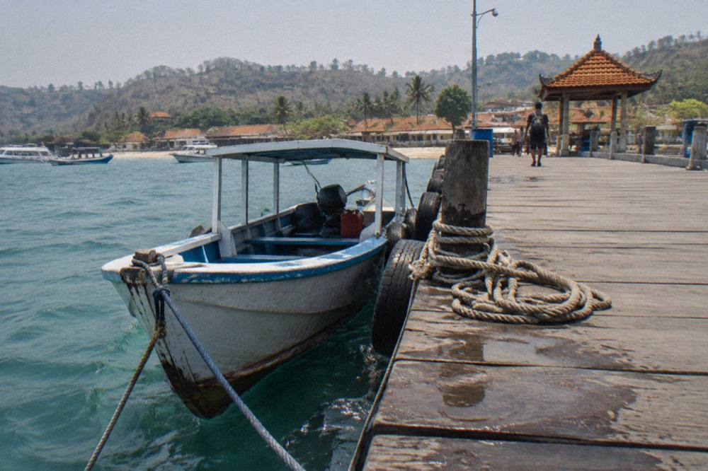 A small boat moored at a wooden jetty on the Nusa Penida coast