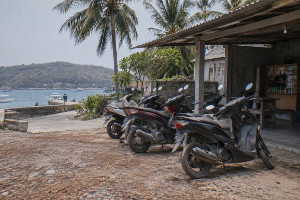 A row of parked scooters beside a small shop on a hillside road