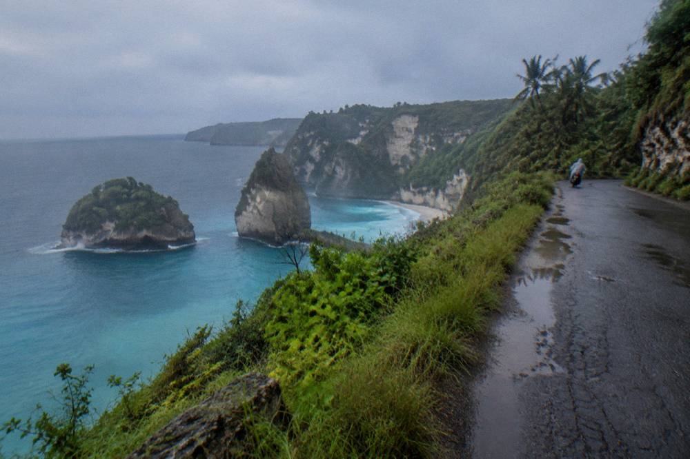 A single lane road curving along a clifftop above turquoise water
