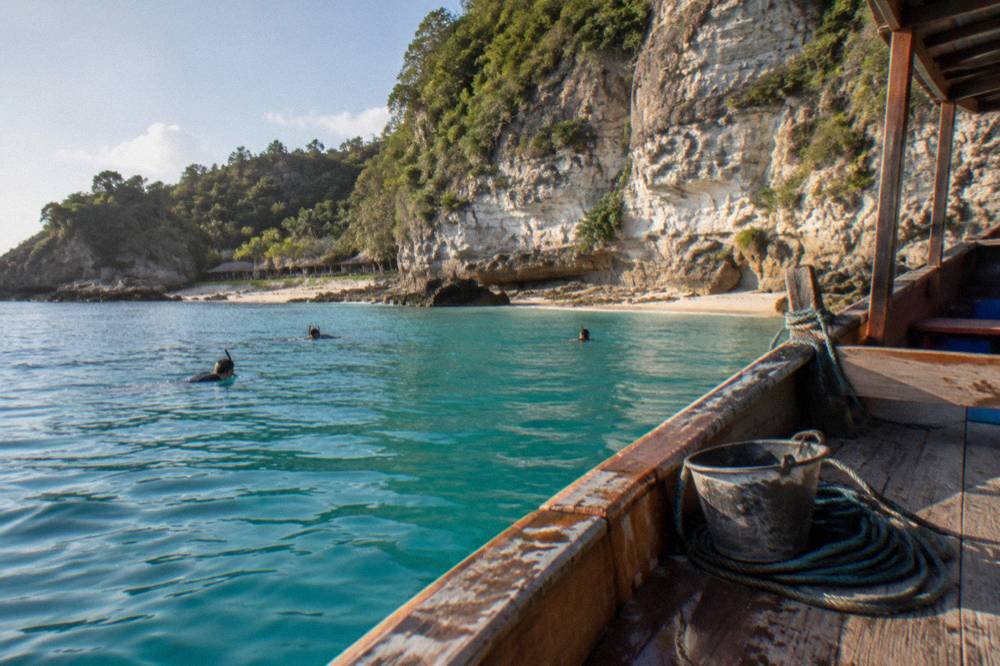 A wooden snorkel boat anchored beside a limestone cliff on a calm bay