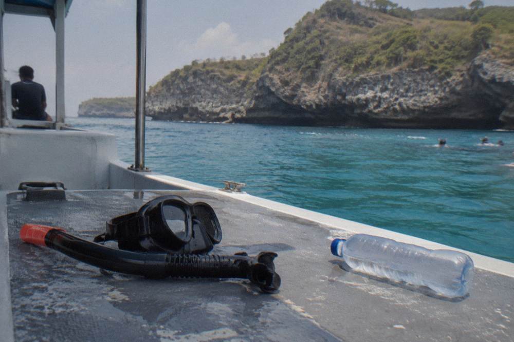 A diver's snorkel and mask resting on a boat deck with turquoise water beyond
