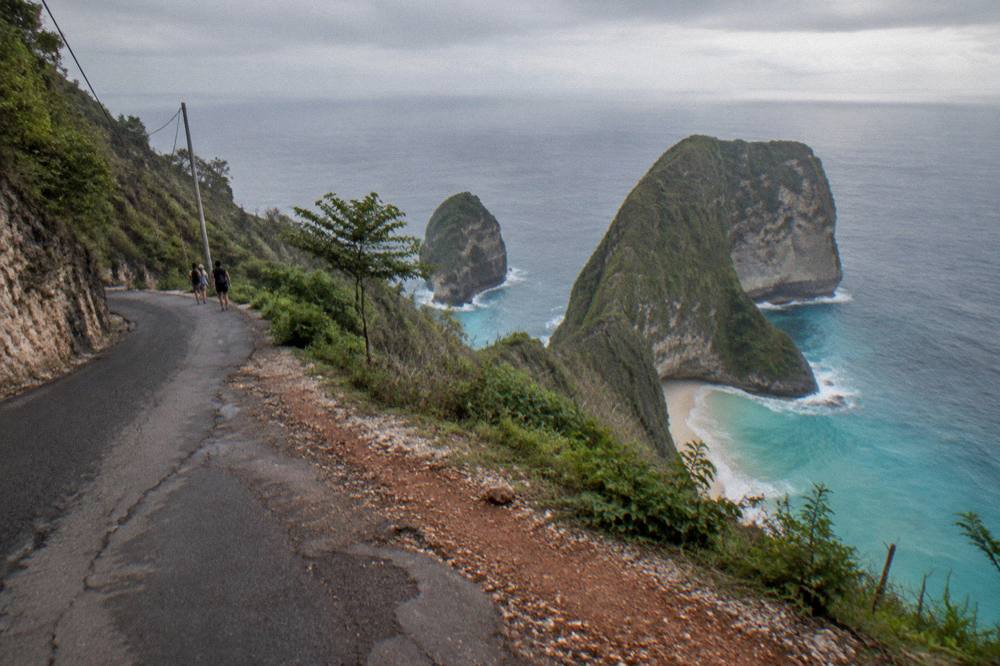 A coastal road winding above turquoise water toward cliffs on a small island