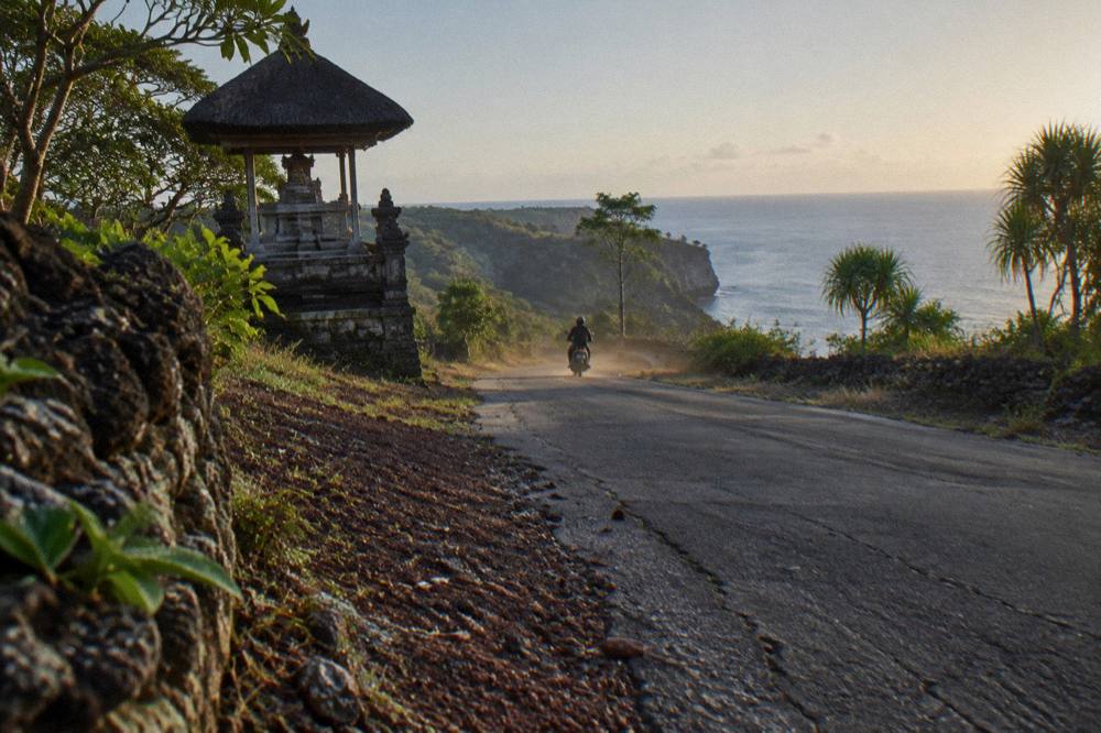 A coastal road winding along the cliffs of Nusa Penida toward the sea