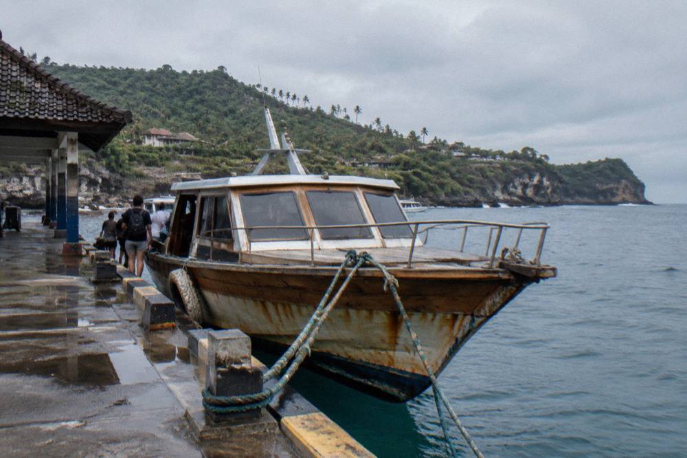 A wooden fast boat moored at a harbour jetty with passengers boarding
