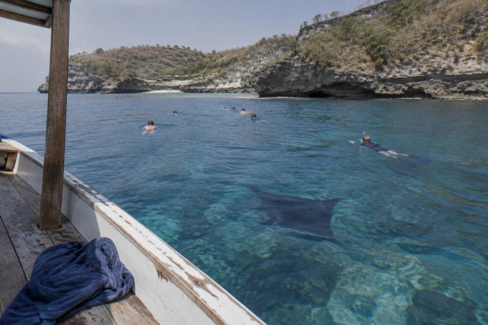 Snorkelers floating above a manta ray in clear blue water near Nusa Penida