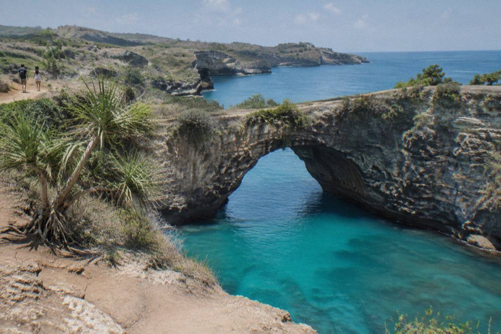 Sunlit turquoise water breaking against the limestone arch at Broken Beach on a calm dry-season day