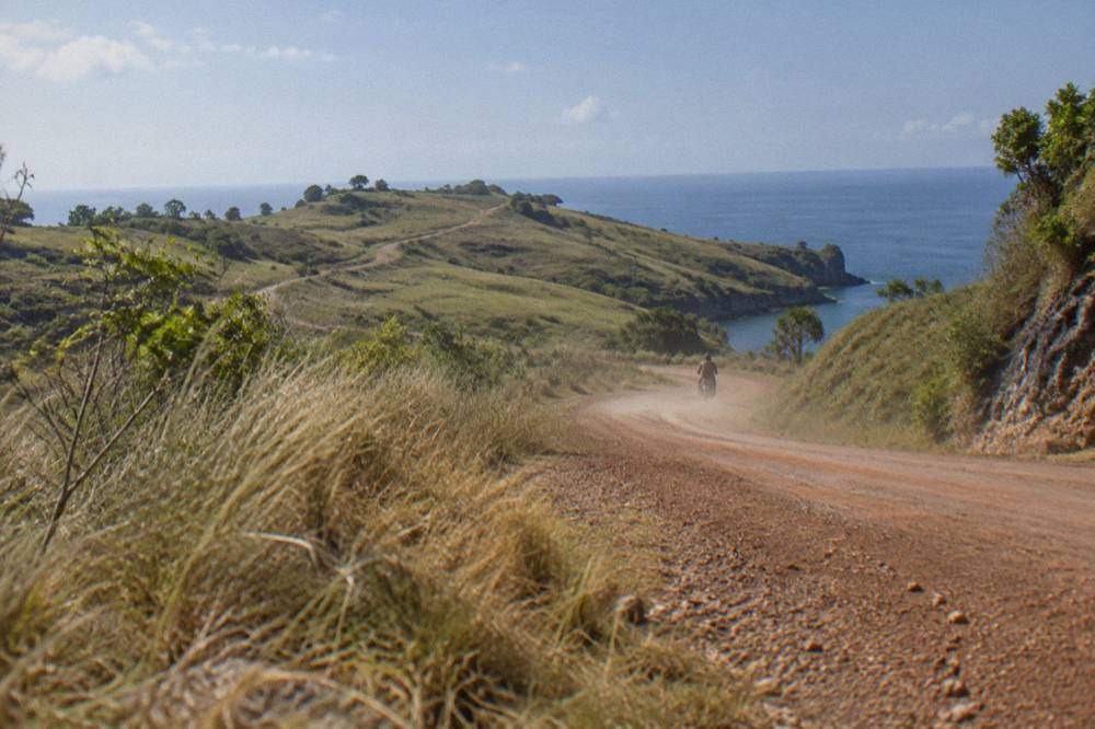 An open coastal road on Nusa Penida curving past dry grass and a calm sea horizon